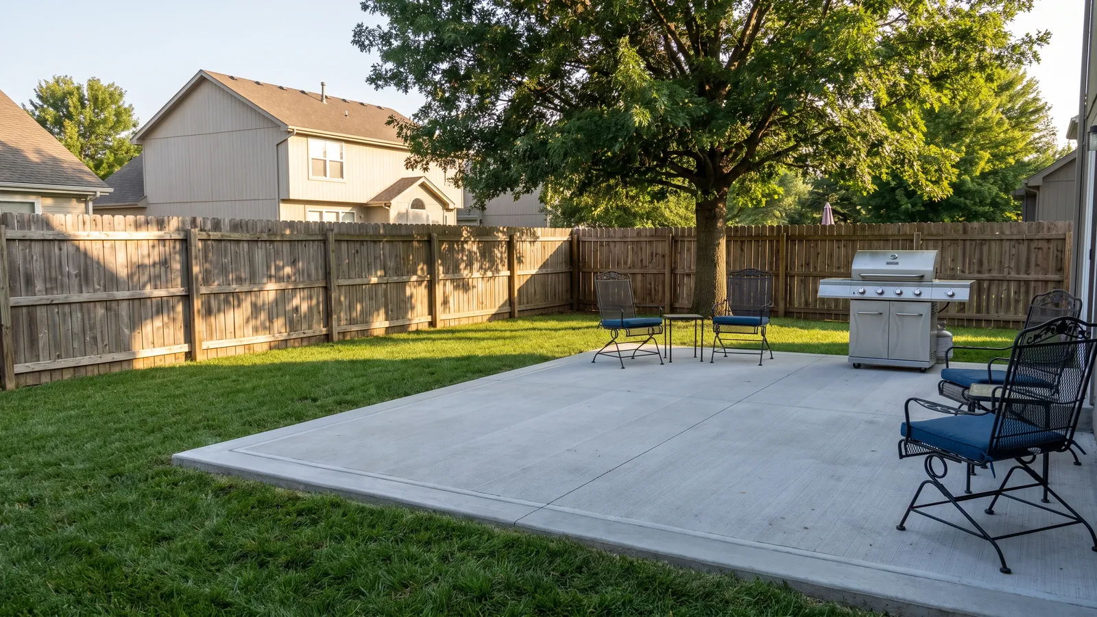 Broom-finish concrete patio with a smooth troweled border behind an Olathe home with a cedar privacy fence, patio furniture and a green lawn